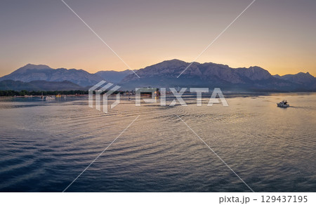 Seascape sunset panorama over the Mediterranean Sea near Kemer, Turkey. Panoramic view to the moonlight beach at dusk and a lone boat cruises across the calm water towards the majestic mountains 129437195