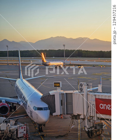 ANTALYA, TURKEY - JULY 5, 2025 Antalya airport scene at sunset and a plane docked at the jet bridge with other aircrafts visible on the tarmac. Distant mountains range silhouette in the background ANTALYA, TURKEY - JULY 5, 2025 Antalya airport scene at sunset and a plane docked at the jet bridge with other aircrafts visible on the tarmac. Distant mountains range silhouette in the background 129437216