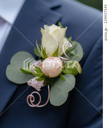 Close-up of floral boutonniere with roses and eucalyptus on grooms navy blue suit during a wedding ceremony. Close-up of floral boutonniere with roses and eucalyptus on grooms navy blue suit during a wedding ceremony. 129437345