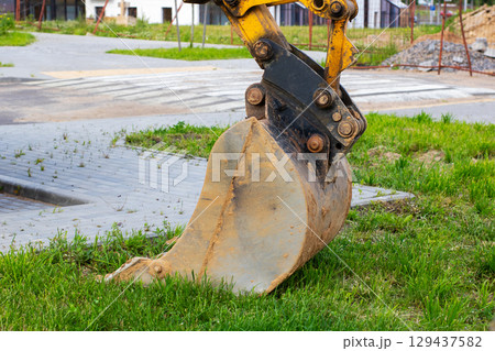 A bright yellow excavator bucket is resting on the green grass A bright yellow excavator bucket is resting on the green grass 129437582