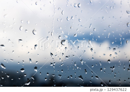Rain drops softly bead on a window, while a cloudy sky looms overhead 129437622