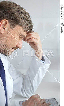 Confident male mature scientist is thinking and analyzing data on a tablet in his laboratory, with a microscope in the background, suggesting advanced scientific research. Medicine and science concept Confident male mature scientist is thinking and analyzing data on a tablet in his laboratory, with a microscope in the background, suggesting advanced scientific research. Medicine and science concept 129437900