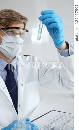 Male scientist in protective gear analyzing a test tube of turquoise liquid with a pipette in a modern laboratory setting. Medicine, and science concept Male scientist in protective gear analyzing a test tube of turquoise liquid with a pipette in a modern laboratory setting. Medicine, and science concept 129437901