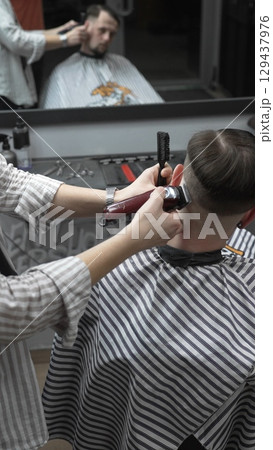 Professional barber grooming client's hair using electric clipper, delivering precise cut with skill in contemporary salon setting Professional barber grooming client's hair using electric clipper, delivering precise cut with skill in contemporary salon setting 129437976