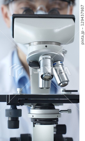 Scientist wearing lab coat and protective glasses using a modern microscope in a laboratory setting, conducting research and experiments in a scientific environment. Health care and science concept Scientist wearing lab coat and protective glasses using a modern microscope in a laboratory setting, conducting research and experiments in a scientific environment. Health care and science concept 129437987