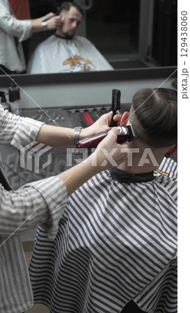 Professional barber grooming client's hair using electric clipper, delivering precise cut with skill in contemporary salon setting 129438060