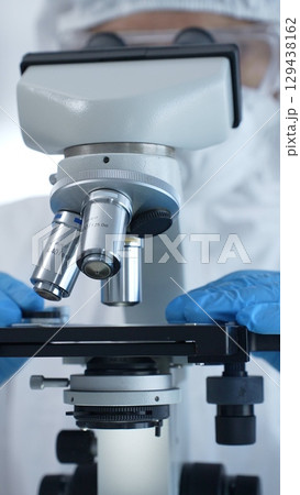 Medical virologist in a hazmat suit, mask, and gloves, diligently working at a microscope in a laboratory researching viruses. Healthcare and science concept 129438162