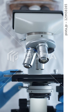 Medical virologist in a hazmat suit, mask, and gloves, diligently working at a microscope in a laboratory researching viruses. Healthcare and science concept 129438165