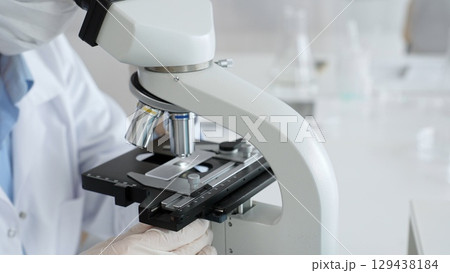 White gloved hands of scientist professional adjusting a microscope in a bright laboratory, emphasizing precision and focus in scientific research. Medicine, healthcare and science concept 129438184