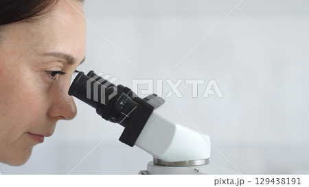 Female scientist peering into microscope, analyzing biological sample with precision in sterile laboratory research environment. Medicine and science concept 129438191