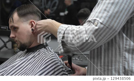 Professional barber trimming customer's hair with electric clipper, focusing on precise nape grooming within contemporary barbershop interior design 129438506