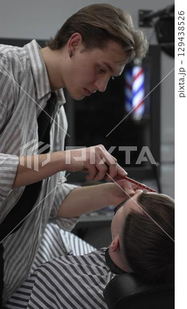 Professional barber trimming customer's hair with electric clipper, focusing on precise nape grooming within contemporary barbershop interior design 129438526
