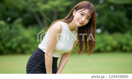 緑の芝生の上で前かがみになって微笑むノースリーブの女性 129439085