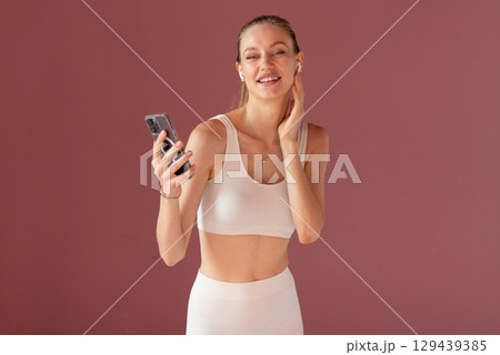 Sporty woman with headphones and smartphone using fitness app for workout guidance. Standing outdoors, enjoying healthy lifestyle and active training session. Sporty woman with headphones and smartphone using fitness app for workout guidance. Standing outdoors, enjoying healthy lifestyle and active training session. 129439385