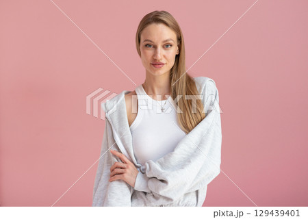 Young woman poses in gray loungewear against pastel pink wall 129439401