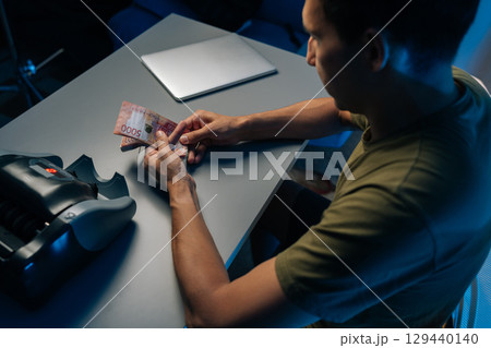 Top view from shoulder of cashier male counting Russian rubles banknotes late at night after closing store using money counting machine in background. Concept of financial accounting in modern office. Top view from shoulder of cashier male counting Russian rubles banknotes late at night after closing store using money counting machine in background. Concept of financial accounting in modern office. 129440140