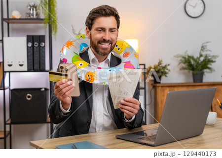 Middle-aged businessman pays for beach holiday tickets smiles closes laptop puts inflatable ring joy 129440173