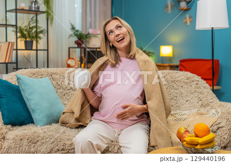 Pregnant woman in blanket sipping herbal tea humming lullaby to baby enjoying cozy soft calm evening Pregnant woman in blanket sipping herbal tea humming lullaby to baby enjoying cozy soft calm evening 129440196