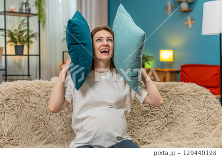 Pregnant woman tries relaxing but neighbors knock sofa shows stop gesture covers ears with pillows 129440198
