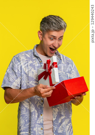 Adult man opening gift box, freezing with amazed happy face showing surprise joy unexpected present Adult man opening gift box, freezing with amazed happy face showing surprise joy unexpected present 129440243