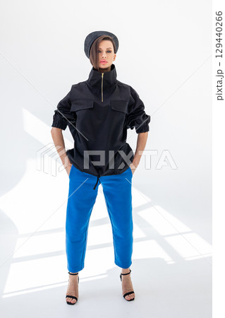 Elegant woman in black windbreaker jacket, blue pants and nautical hat on white background. Fashionable female in ocean French style. Studio photography. Vertical photo. High quality photo Elegant woman in black windbreaker jacket, blue pants and nautical hat on white background. Fashionable female in ocean French style. Studio photography. Vertical photo. High quality photo 129440266