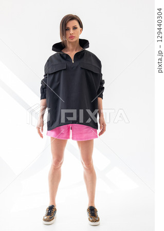 Elegant woman in black windbreaker jacket and pink shorts on light background. Fashionable female style. Studio photography. Vertical photo. High quality photo 129440304
