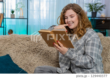 Woman sitting on sofa opening and reading book with focus thoughtfully flipping pages and reflecting 129440377