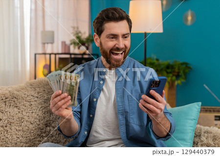Man checking balance on smartphone, excited about received money, celebrating lottery or game win 129440379