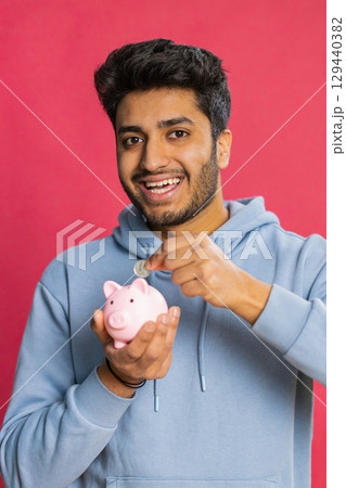 Happy Indian man holding piggy bank saving money dropping coins planning future financial security 129440382