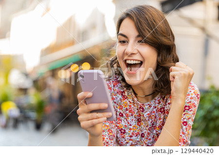 Happy woman use mobile smartphone celebrating win good message news outdoors in urban city street Happy woman use mobile smartphone celebrating win good message news outdoors in urban city street 129440420