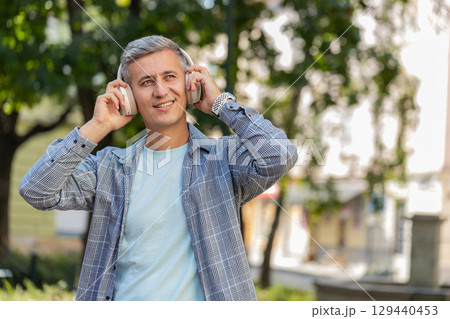 Young gray-haired man listening to music using wireless headphones and smartphone on city street Young gray-haired man listening to music using wireless headphones and smartphone on city street 129440453