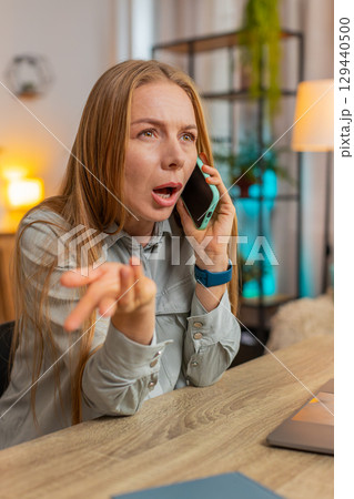 Angry Caucasian mature businesswoman freelancer talking on smartphone sitting at home office table 129440500