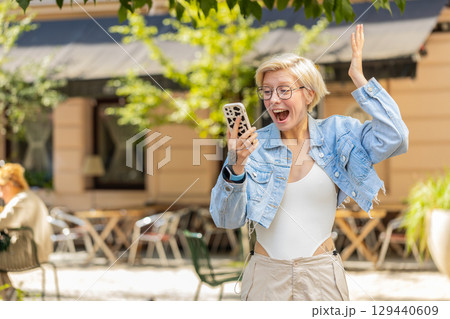 Excited European woman using mobile phone typing browsing celebrating win on urban city street Excited European woman using mobile phone typing browsing celebrating win on urban city street 129440609