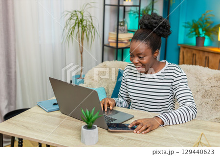 African American woman analyzing cryptocurrency charts laptop table phone indoors focused notes African American woman analyzing cryptocurrency charts laptop table phone indoors focused notes 129440623