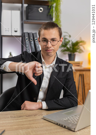 Upset young Caucasian businessman freelancer showing double thumbs down sitting at home office desk 129441031
