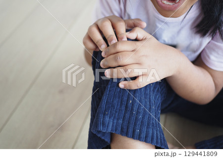Child suffering knee joint pain sitting on floor  129441809