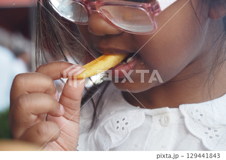 Young girl enjoying a crispy snack during family outing 129441843
