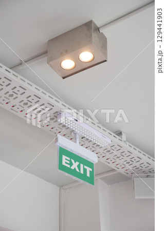Bright exit sign under ceiling lights in a public space 129441903