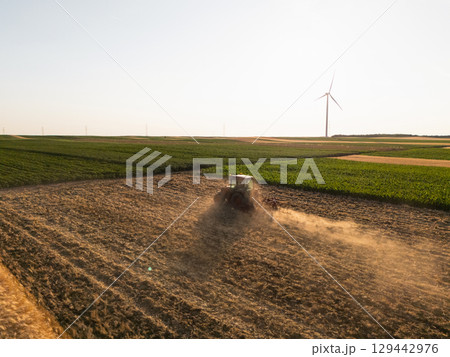Agricultural tractor is working on the field with wind turbines. Aerial view. 129442976