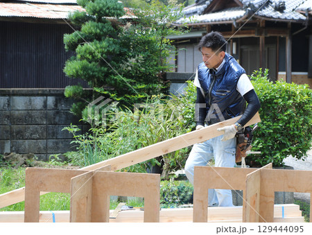 大工さんが使用する木材を持ち上げて作業台に載せようとしている 129444095