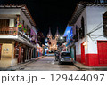 Street lined with colorful colonial buildings leads to the illuminated Basilica of the Immaculate Conception at night in Jardin, Colombia 129444097