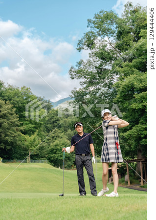 ゴルフ場でゴルフを教えるゴルファーの男性とティーショットを打つ女性ゴルファー ゴルフ場でゴルフを教えるゴルファーの男性とティーショットを打つ女性ゴルファー 129444406