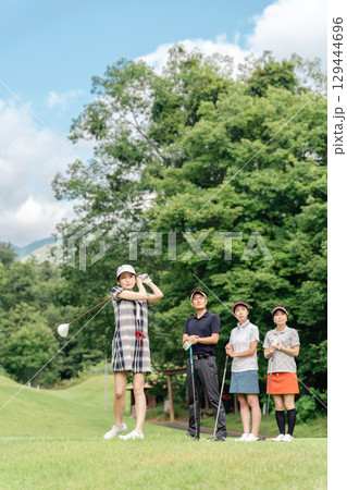 ゴルフ場でティーショットを打つ女性ゴルファーとスイングを見る同伴のゴルファー 129444696