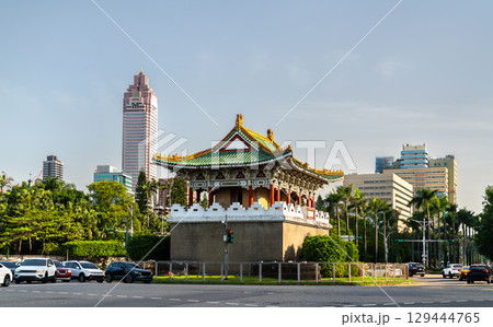 East Gate, a traditional Chinese-style gate tower with green tiles and ornate architecture stands at a roundabout in central Taipei, Taiwan, surrounded by palm trees and urban buildings under a clear 129444765