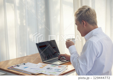 Asian Businessman using laptop calling phone at office desk. Man wear eye glasses talking smartphone read financial graph chart Planning marketing info. Happy Asian business people work office firm 129444772