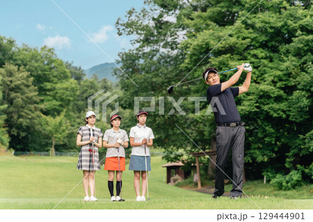 ゴルフ場でティーショットを打つ男性ゴルファーとスイングを見る同伴のゴルファー 129444901