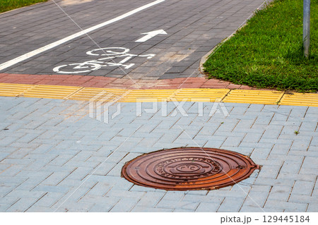 There is a manhole cover located on the sidewalk beside a bike lane 129445184