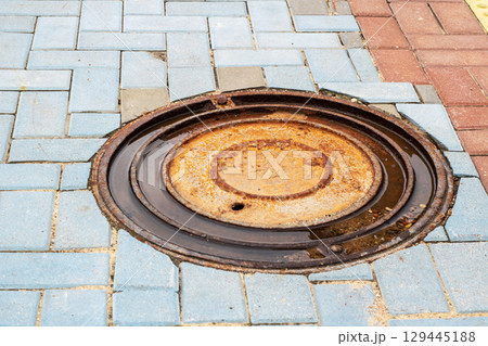 A worn and rusty manhole cover sitting on a brick sidewalk 129445188