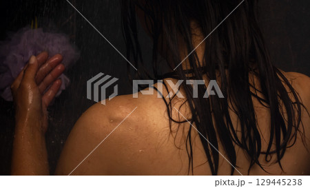 A woman is taking a shower while holding a sponge in her hand 129445238