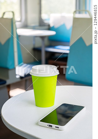 Focus on a green eco cup and a smartphone on a table inside a train for a solo travel trip. Focus on a green eco cup and a smartphone on a table inside a train for a solo travel trip. 129446815